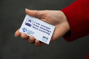 A person holding the Scottish Government face covering exemption card featuring healthier Scotland logo and NHS Scotland logo