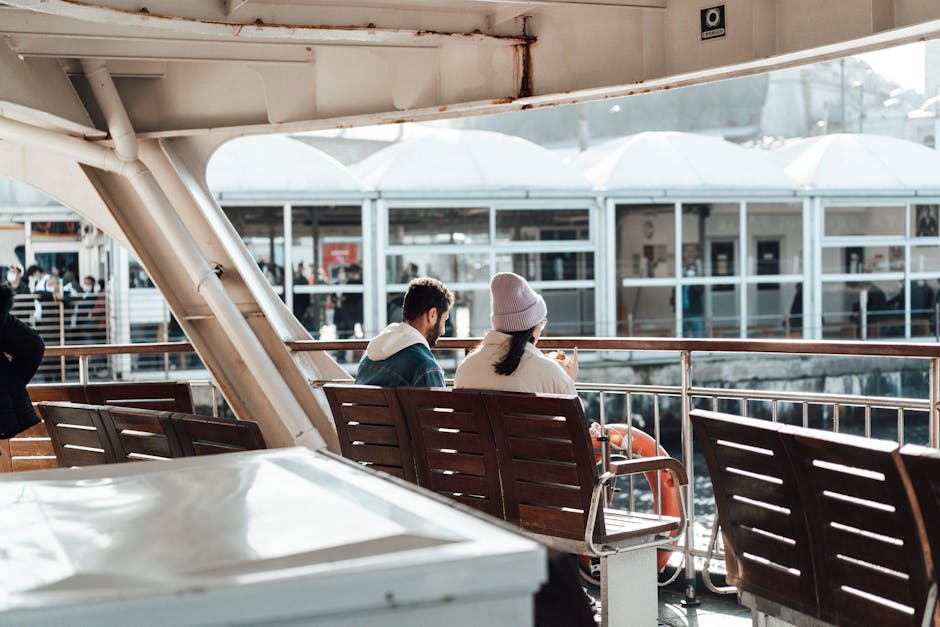 A view of the back of a man and woman sitting on a bench looking over the railing of a ship